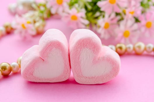 sweet heart shape of marshmallows with flower on pink background.