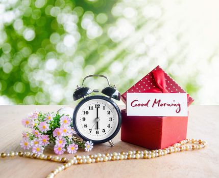 Good morning tag and alarm clock with gift box on spring background.
