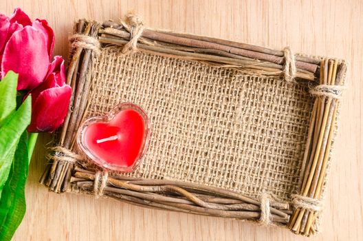 Red candle glass in sack photo frame with red tulip on wooden background.