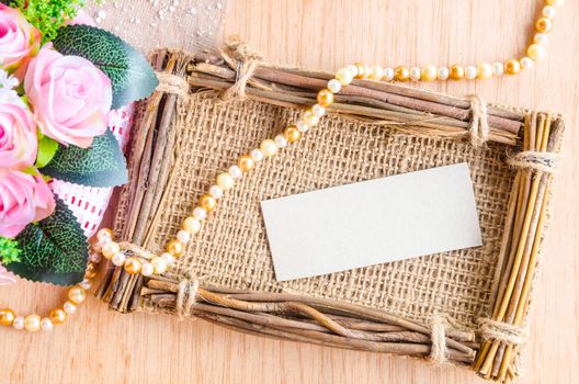 Blank paper tag in sack photo frame with beautiful flower on wooden background.