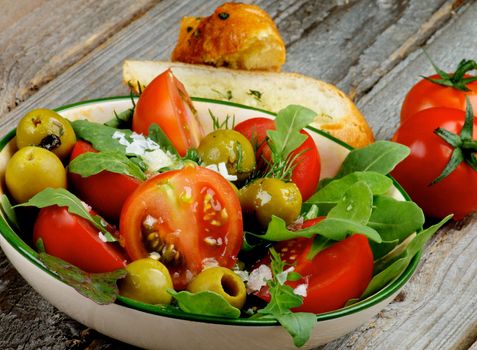 Fresh Tomatoes Salad with Arugula, Olives, Greens, Sea Salt and Garlic Bread isolated on Rustic Wooden background