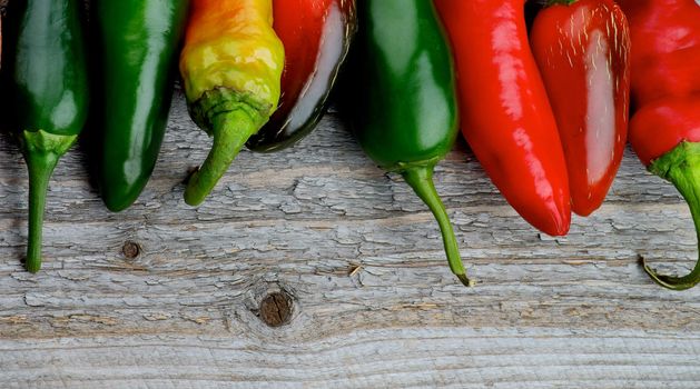 Horizontal Frame of Various Red and Green Habanero and Jalapeno Chili Peppers with Stems on Rustic Wooden background