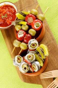 Delicious Spanish Snacks with Stuffed Small Peppers, Anchovies, Green Olives and Tomatoes Sauce with Bread Sticks in Various Bowls closeup on Green Napkin. Top View