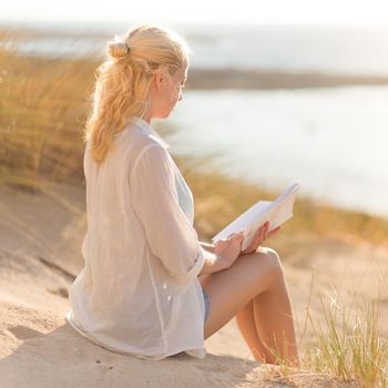 Relaxed woman enjoys reading on beautiful sandy beach.  Young lady with book in her hand. Concept of happiness, enjoyment and well being.  Enjoying Sun on Vacations. 