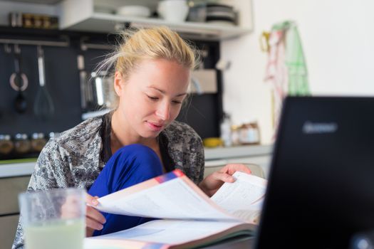 Female freelancer in her casual home clothing working remotly from her dining table in the morning. Home kitchen in the background.