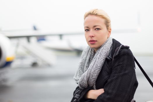 Casually dressed young stylish female traveller boarding airplane in cold winter weather wearing winter coat and wool scarf. Woman on Business travel.