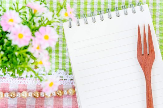 Open diary and wooden spoon fork with flower on beautiful fabric background. Menu concept.
