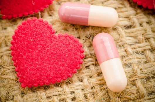 Capsule pill and red heart on sack background.