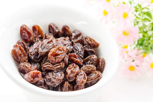 Raisins in a bowl with flower on white background