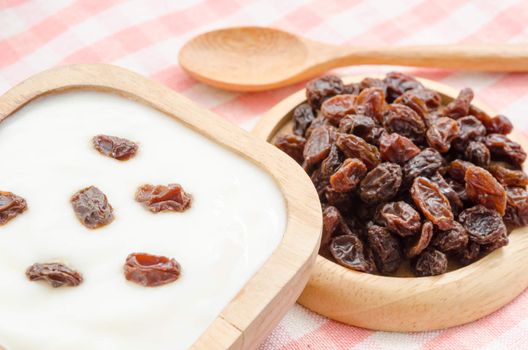 Home sweet yogurt with raisins in a wooden bowl on fabric background.