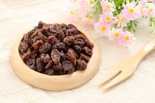 Raisin on wooden dish and wooden fork spoon with flower on vintage fabric background.