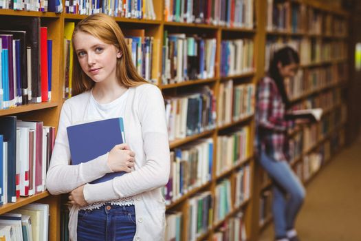 Smiling student leaning against bookshelves at the university