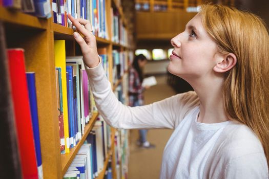 Blond student looking for book in library shelves at the university