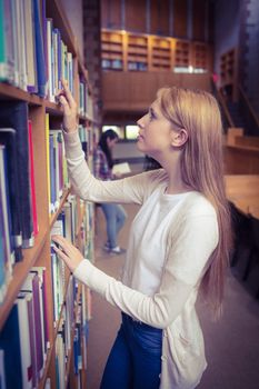 Blond student looking for book in library shelves at the university