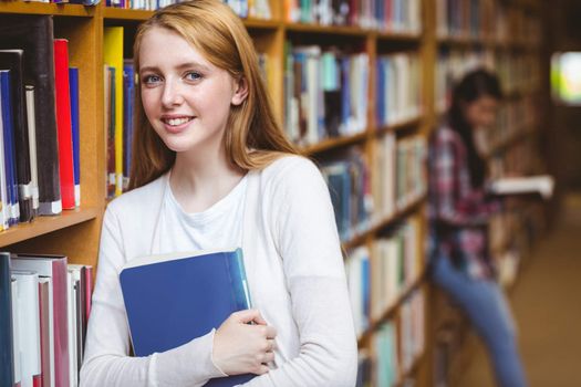 Smiling student leaning against bookshelves at the university