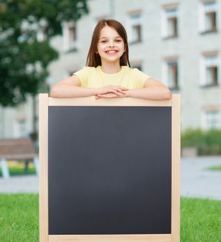 people, advertisement and education concept - happy little girl with blank blackboard