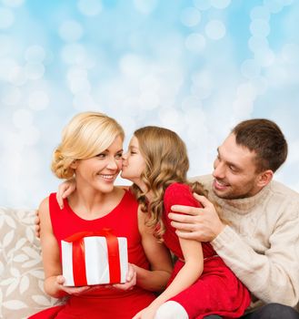 christmas, holidays, family and people concept - happy mother, father and little girl with gift box kissing over blue lights background