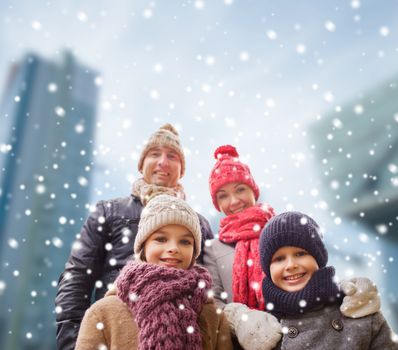family, childhood, season and people concept - happy family in winter clothes over snowy city background