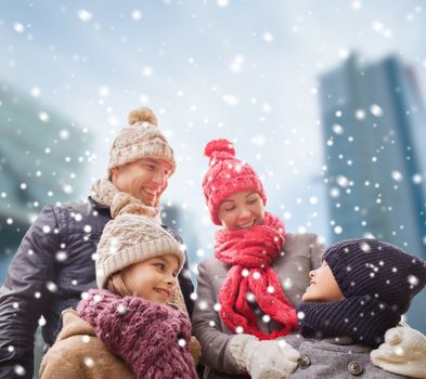 family, childhood, season and people concept - happy family in winter clothes over snowy city background