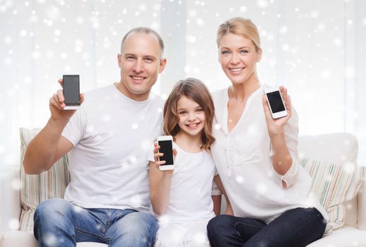 holidays, technology, advertisement and people concept - smiling family showing smartphones blank screens over snowflakes background