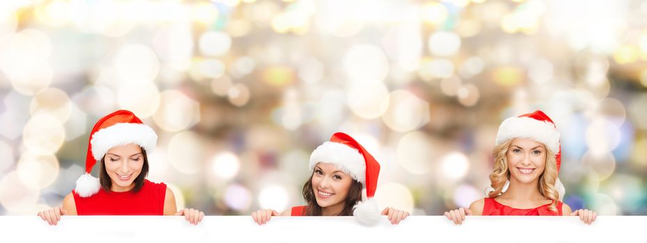 christmas, x-mas, people, advertisement and sale concept - happy women in santa helper hat with blank white board over lights background