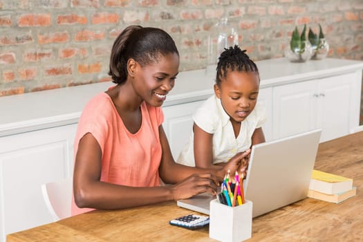 Cute daughter using laptop at desk with mother in living room