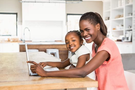 Cute daughter using laptop at desk with mother in living room