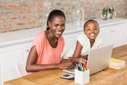 Cute daughter using laptop at desk with mother in living room