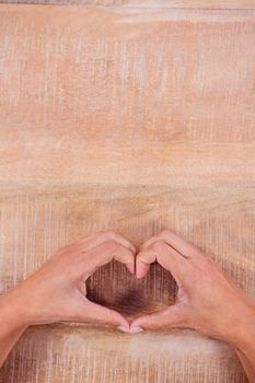 View of hands making heart shape on wooden desk