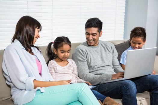 Smiling family on the sofa using laptop and tablet