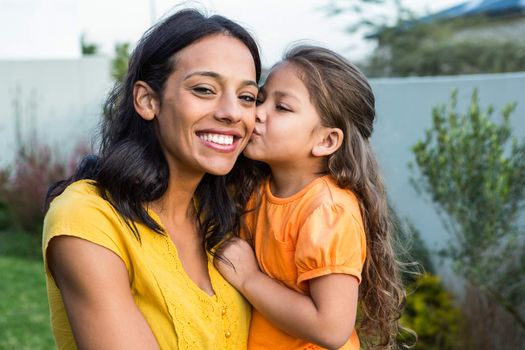 Cute daughter kissing her mothers cheek outdoors