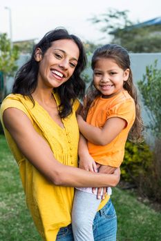 Standing mother holding her daughter outdoors posing for the camera