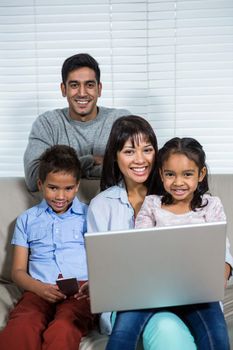 Smiling family using laptop and smartphone on the sofa in living room