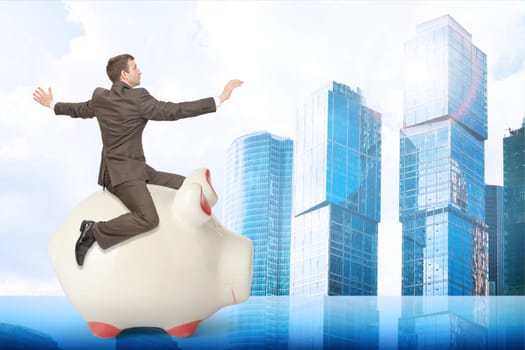 Businessman sitting on piggy bank on city background