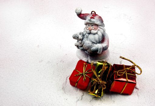 Christmas decoration, snowy figure of Santa Claus holding in his arms a little lamb and three decorative gifts .Horizontal view.