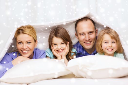 family, children, comfort, bedding and home concept - happy family with two kids under blanket over snowflakes background