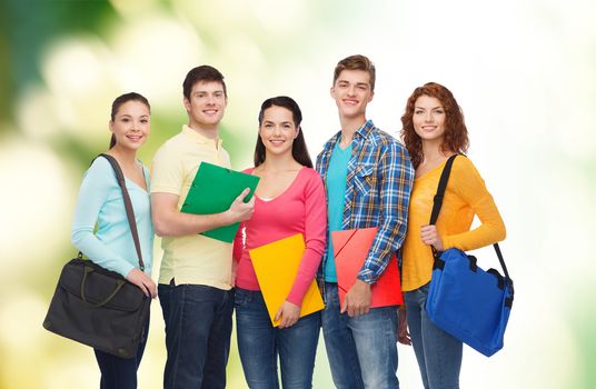 friendship, ecology, education and people concept - group of smiling teenagers with folders and school bags over green background