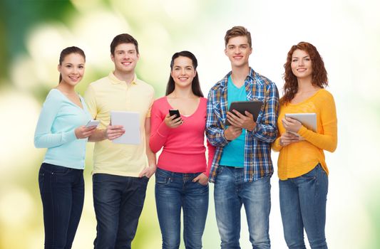 friendship, technology and people concept - group of smiling teenagers with smartphones and tablet pc computers over green background