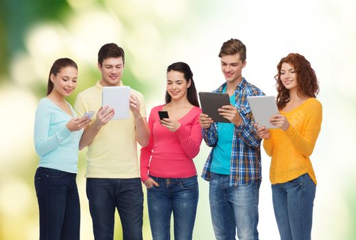 friendship, technology and people concept - group of smiling teenagers with smartphones and tablet pc computers over green background