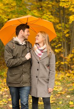 love, relationship, season, family and people concept - smiling couple with umbrella walking in autumn park