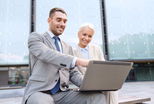 business, education, technology and people concept - smiling businesspeople working with laptop computer on city street