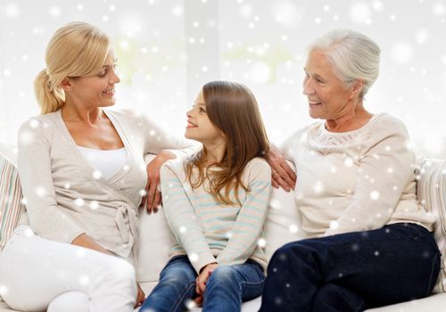 family, happiness, generation and people concept - smiling mother, daughter and grandmother sitting on couch at home