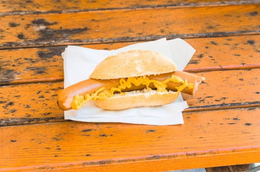 Sausage with mustard on buns. The sausage is on a brown wooden table.