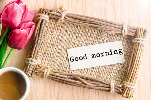 Good morning paper tag in sack photo frame and coffee with red tulip on wooden background.