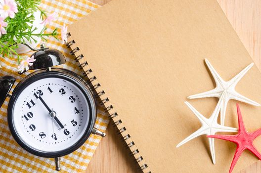 Brown diary and alarm clock with flower on wooden background.