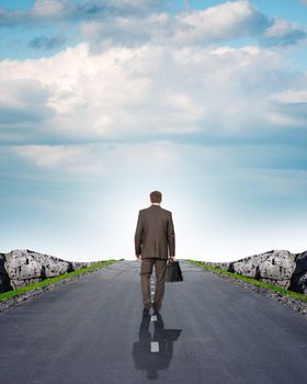 Businessman on road with mountains and blue sky, rear view