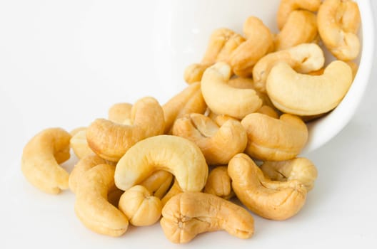 Raw cashews close-up in white bowl on white background.