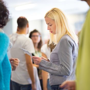 Young blond caucsian woman waiting in line with plain ticket in her hands. Lady standing in a long queue to board a plane.