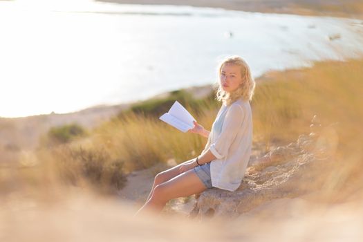 Relaxed woman enjoys reading on beautiful sandy beach.  Young lady with book in her hand. Concept of happiness, enjoyment and well being.  Enjoying Sun on Vacations. 