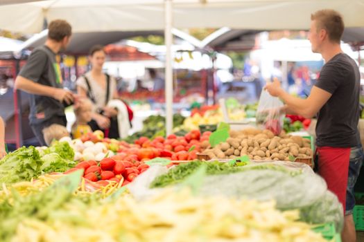 Farmers' food market stall with variety of organic vegetable. Vendor serving and chating with customers.